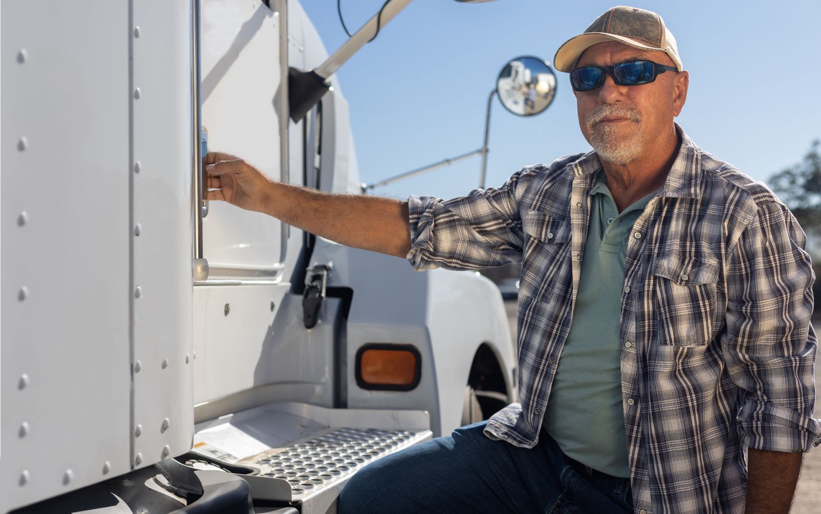 An experienced truck driver stands at the door of his cab